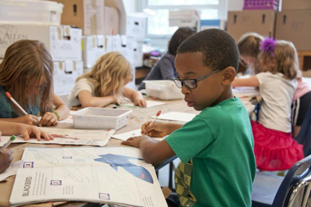 Several kids drawing at a table in school.